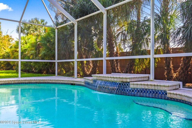 view of pool featuring a hot tub, pool water feature, and glass enclosure