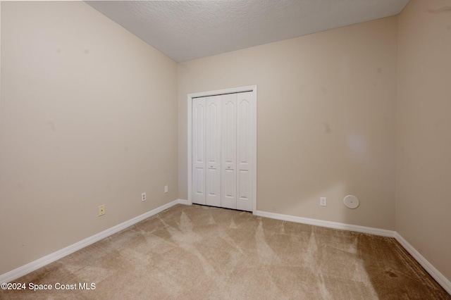 unfurnished bedroom with light carpet, a textured ceiling, and a closet