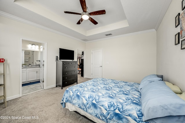 bedroom with ceiling fan, light carpet, a raised ceiling, ensuite bath, and ornamental molding