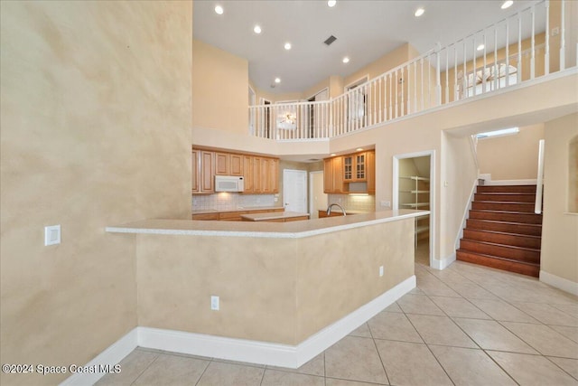 kitchen with a high ceiling, kitchen peninsula, light tile patterned floors, and tasteful backsplash