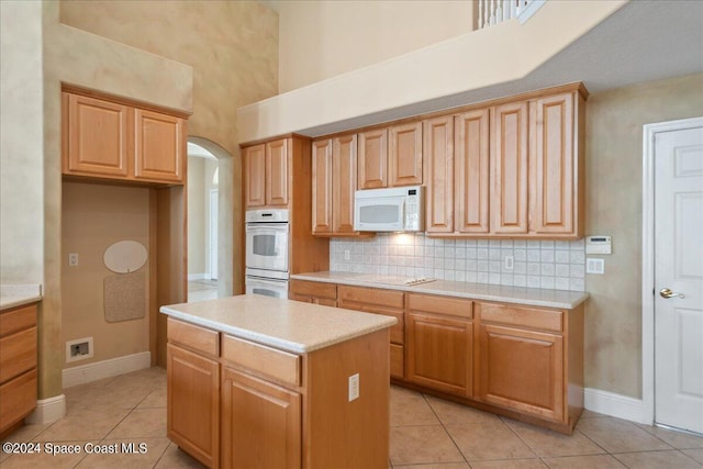 kitchen featuring white appliances, a center island, light tile patterned floors, and tasteful backsplash