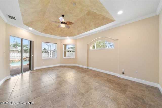 spare room with ceiling fan, a tray ceiling, crown molding, and light tile patterned floors