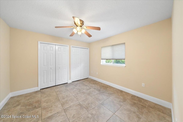 unfurnished bedroom with ceiling fan, a textured ceiling, two closets, and light tile patterned flooring