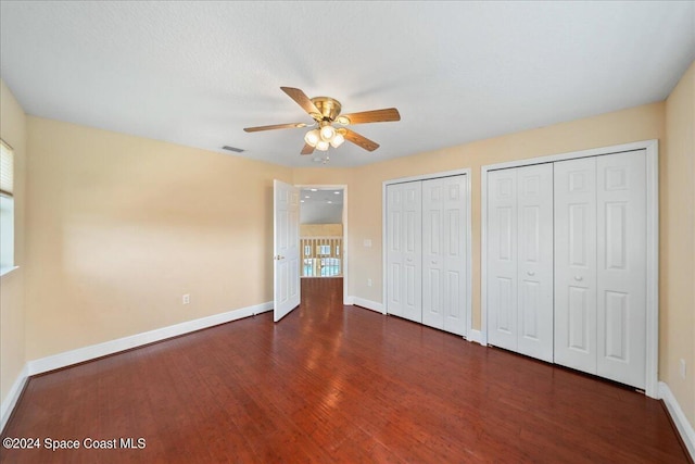 unfurnished bedroom featuring ceiling fan, dark wood-type flooring, and two closets