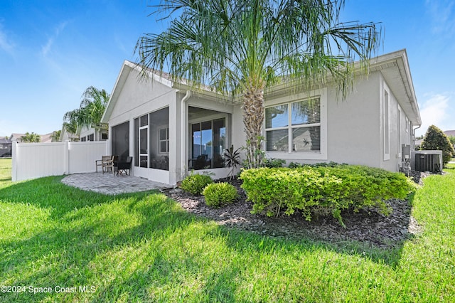 rear view of house featuring a patio area, cooling unit, a sunroom, and a lawn