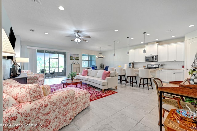 living room featuring ceiling fan with notable chandelier, light tile patterned floors, and a textured ceiling