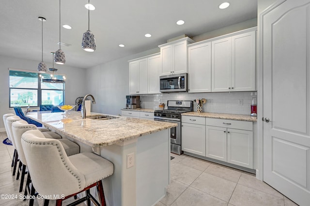 kitchen with a kitchen island with sink, sink, hanging light fixtures, white cabinets, and appliances with stainless steel finishes