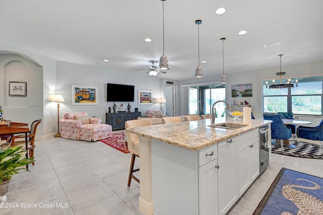 kitchen with an island with sink, light stone counters, white cabinets, sink, and pendant lighting