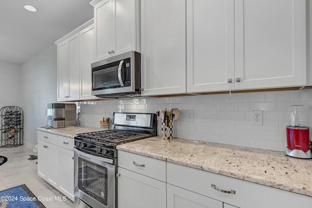 kitchen featuring light stone countertops, stainless steel appliances, baseboards, white cabinets, and decorative backsplash