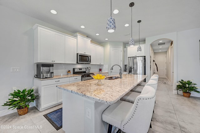 kitchen featuring arched walkways, a breakfast bar area, a sink, appliances with stainless steel finishes, and tasteful backsplash