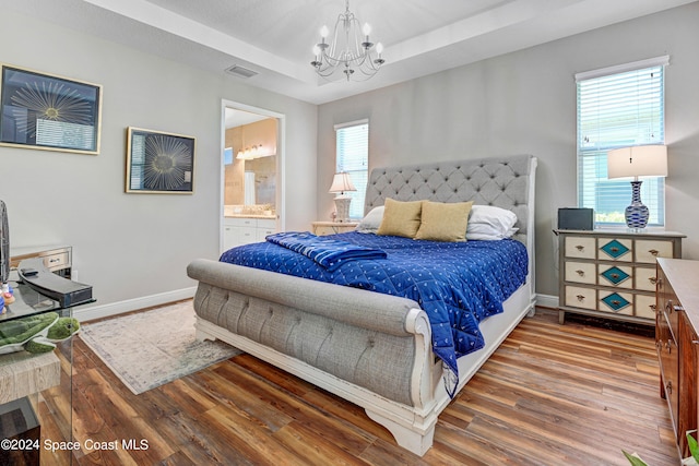 bedroom featuring a tray ceiling, wood finished floors, visible vents, and baseboards