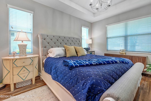 bedroom featuring an inviting chandelier, a raised ceiling, and wood finished floors