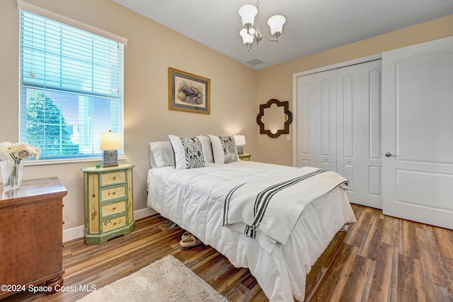 bedroom with a chandelier, wood finished floors, visible vents, baseboards, and a closet