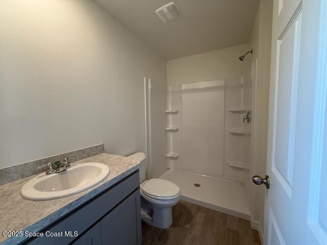 bathroom with hardwood / wood-style flooring, walk in shower, vanity, and toilet