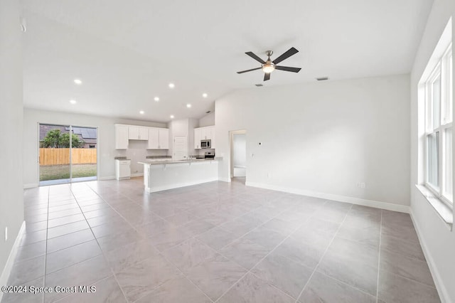 unfurnished living room featuring a wealth of natural light, ceiling fan, light tile patterned flooring, and vaulted ceiling