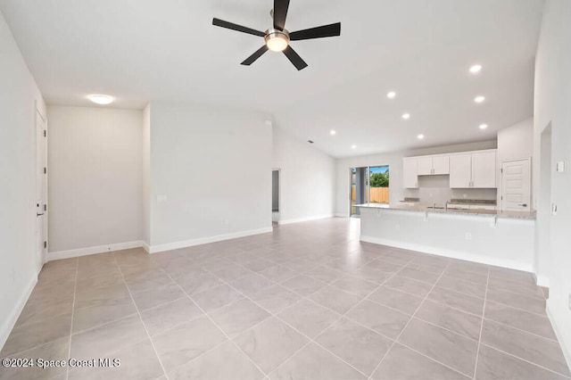 unfurnished living room with ceiling fan, sink, light tile patterned floors, and vaulted ceiling