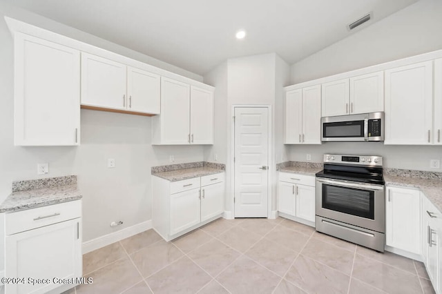 kitchen with light stone countertops, white cabinetry, stainless steel appliances, and vaulted ceiling