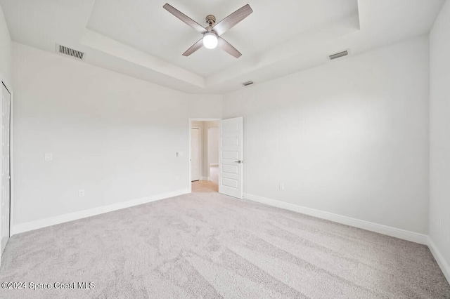 carpeted empty room featuring ceiling fan and a raised ceiling