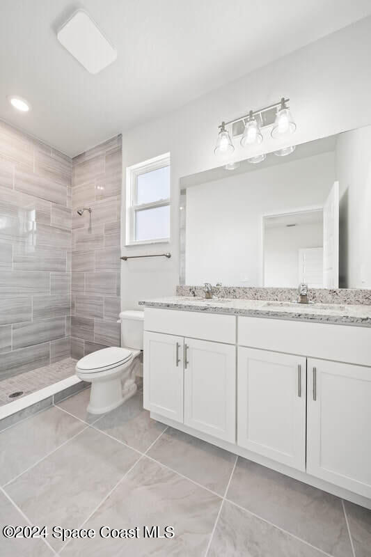 bathroom featuring tiled shower, tile patterned floors, vanity, and toilet