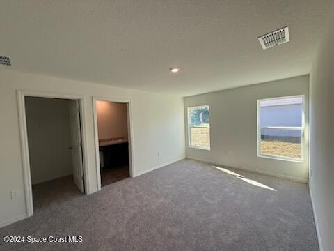 unfurnished bedroom featuring a walk in closet, carpet, and a textured ceiling