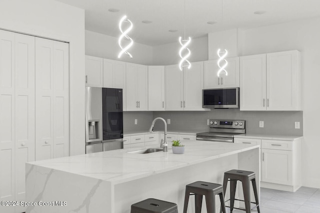 kitchen with an island with sink, sink, hanging light fixtures, white cabinetry, and appliances with stainless steel finishes