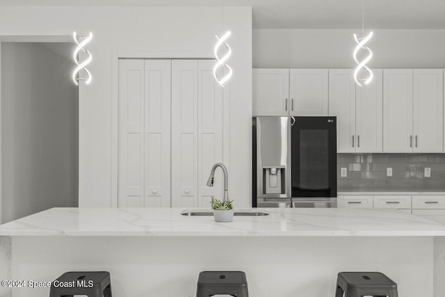 kitchen featuring light stone counters, stainless steel refrigerator with ice dispenser, sink, and white cabinetry