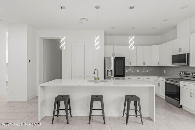 kitchen featuring pendant lighting, a breakfast bar area, a center island with sink, light stone counters, and stainless steel appliances