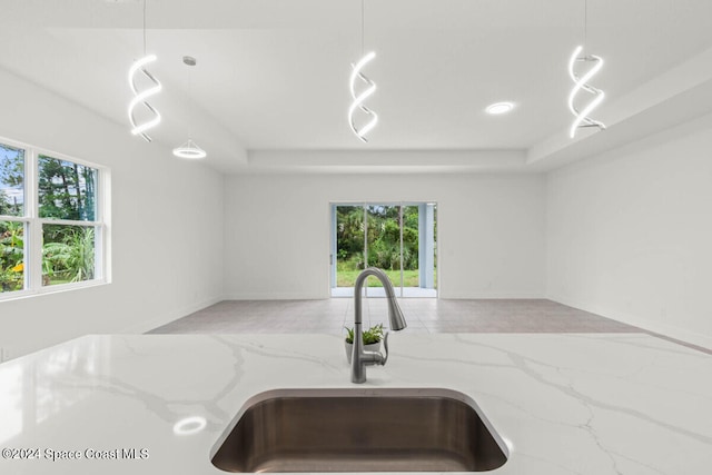 kitchen featuring light stone counters, decorative light fixtures, sink, and a raised ceiling