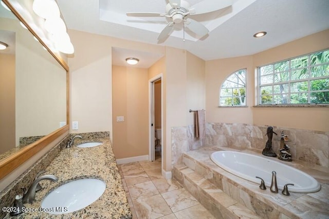 bathroom featuring vanity, toilet, tiled bath, and ceiling fan