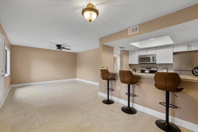 kitchen with backsplash, appliances with stainless steel finishes, a kitchen breakfast bar, white cabinetry, and light stone countertops