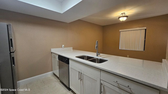 kitchen with kitchen peninsula, stainless steel appliances, sink, light tile patterned flooring, and white cabinetry