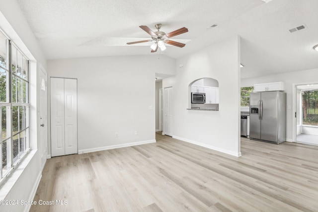 unfurnished living room with ceiling fan, a textured ceiling, vaulted ceiling, and light wood-type flooring