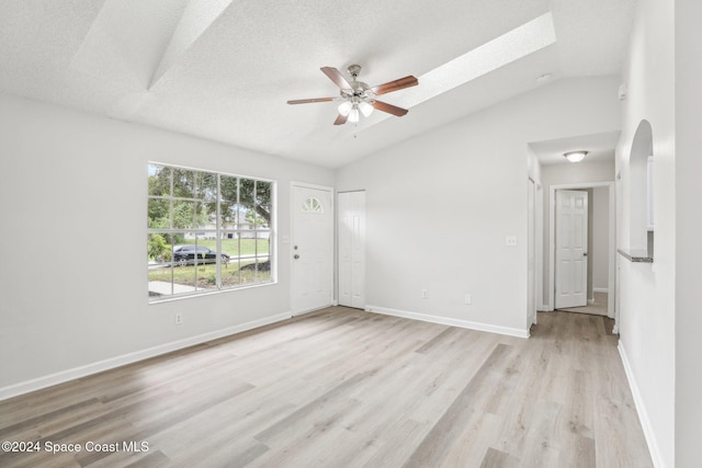 spare room featuring lofted ceiling with skylight, a textured ceiling, light wood-type flooring, and ceiling fan