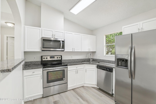 kitchen with appliances with stainless steel finishes, white cabinetry, sink, and vaulted ceiling