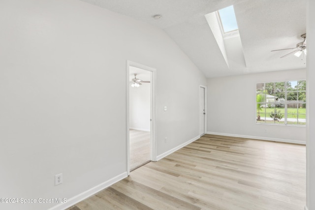 spare room featuring lofted ceiling with skylight, light wood-type flooring, and ceiling fan