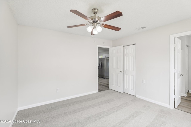 unfurnished bedroom with ensuite bathroom, a closet, ceiling fan, light colored carpet, and stainless steel refrigerator with ice dispenser