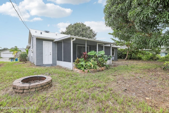 back of house featuring an outdoor fire pit, a lawn, and a sunroom