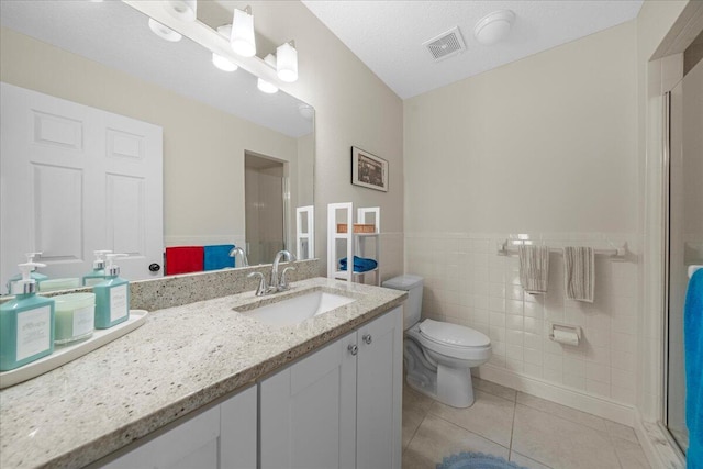 bathroom featuring toilet, walk in shower, tile walls, vanity, and tile patterned flooring