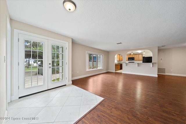 unfurnished living room with light wood-type flooring, a textured ceiling, and french doors