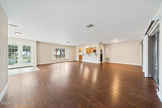 unfurnished living room with a textured ceiling, dark hardwood / wood-style flooring, and french doors