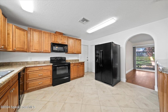 kitchen featuring light stone counters, a textured ceiling, black appliances, and light tile patterned flooring