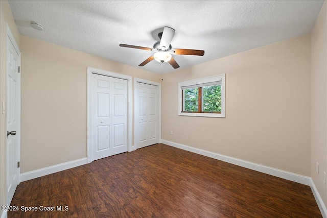 unfurnished bedroom featuring ceiling fan, dark wood-type flooring, a textured ceiling, and two closets