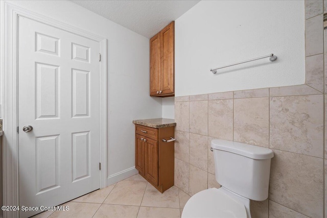 bathroom with a textured ceiling, toilet, tile walls, and tile patterned floors