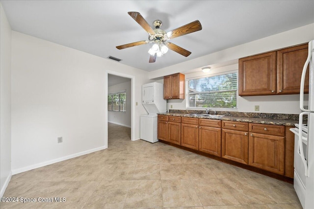 kitchen with stacked washer / drying machine, white fridge, dark stone countertops, sink, and ceiling fan