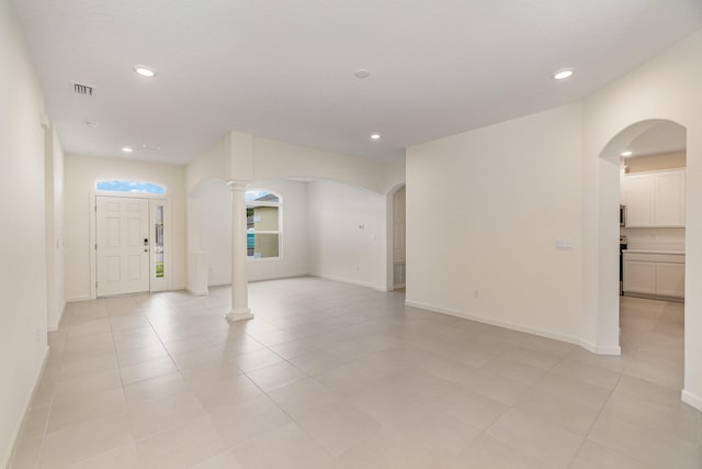 unfurnished room featuring decorative columns and light tile patterned flooring