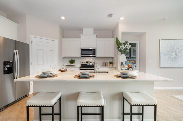 kitchen with stainless steel appliances, a center island with sink, sink, a kitchen bar, and white cabinets