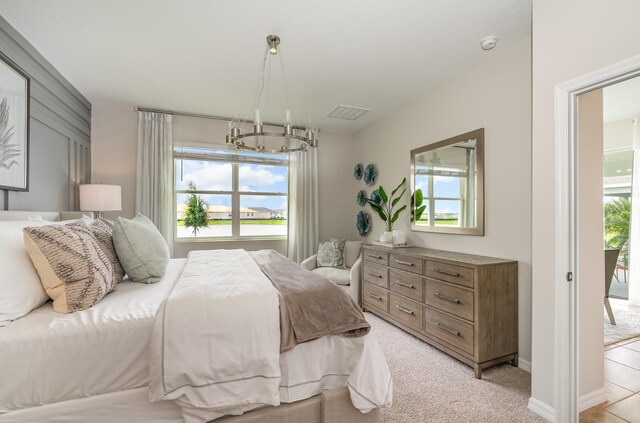 bedroom with light carpet, multiple windows, a chandelier, and access to exterior