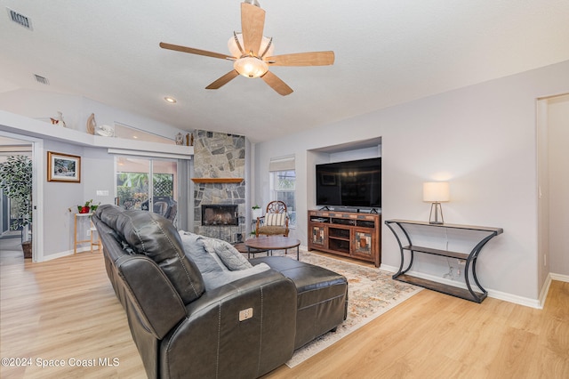 living room with light hardwood / wood-style flooring, lofted ceiling, a stone fireplace, and ceiling fan