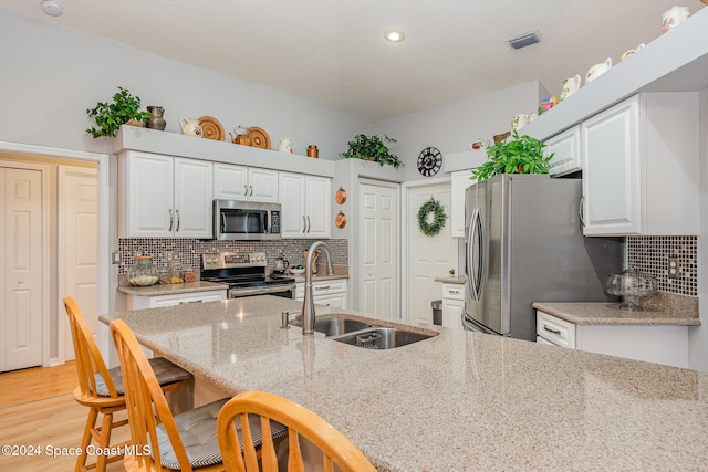 kitchen with light stone countertops, sink, light wood-type flooring, stainless steel appliances, and white cabinets