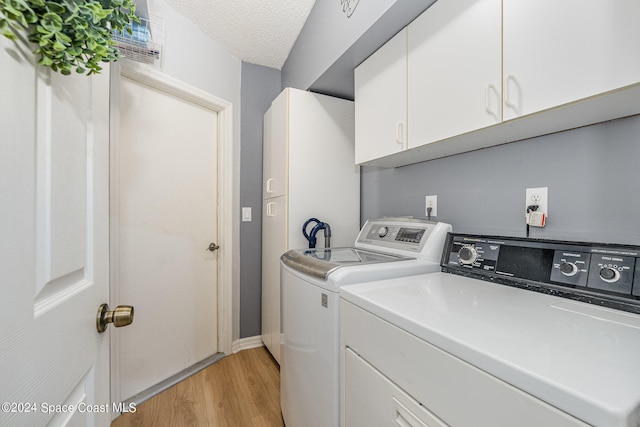 washroom with washer and dryer, a textured ceiling, cabinets, and light wood-type flooring